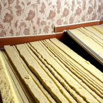 **Image Prompt:** Interior of a typical Russian apartment showing layers of soundproofing material (mineral wool, drywall) being installed on a wall. Show tools like a строительный нож (utility knife) and строительный уровень (spirit level) nearby. Focus on the construction process.